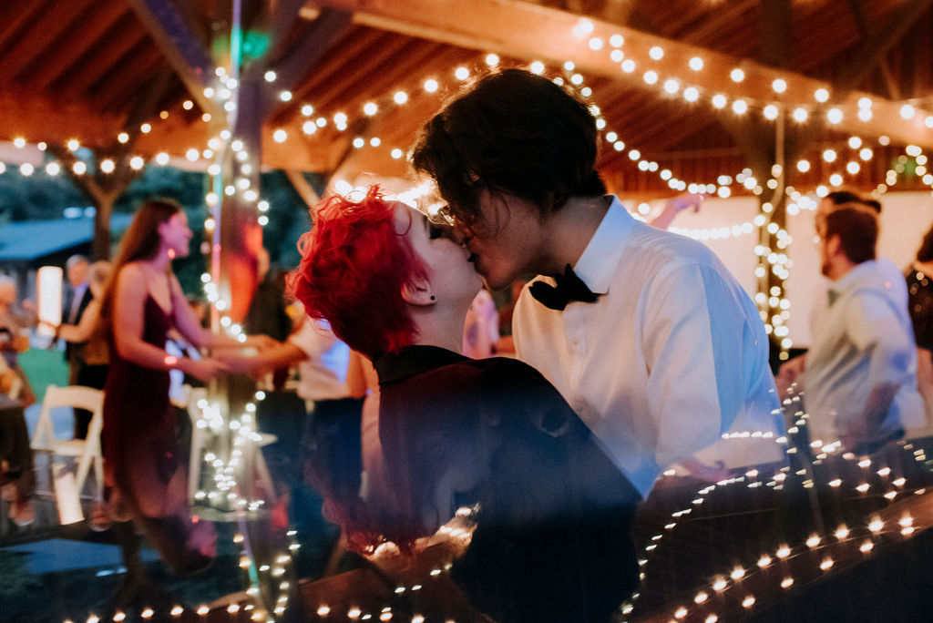 Couple kissing while on the dance floor surrounded by string lights.